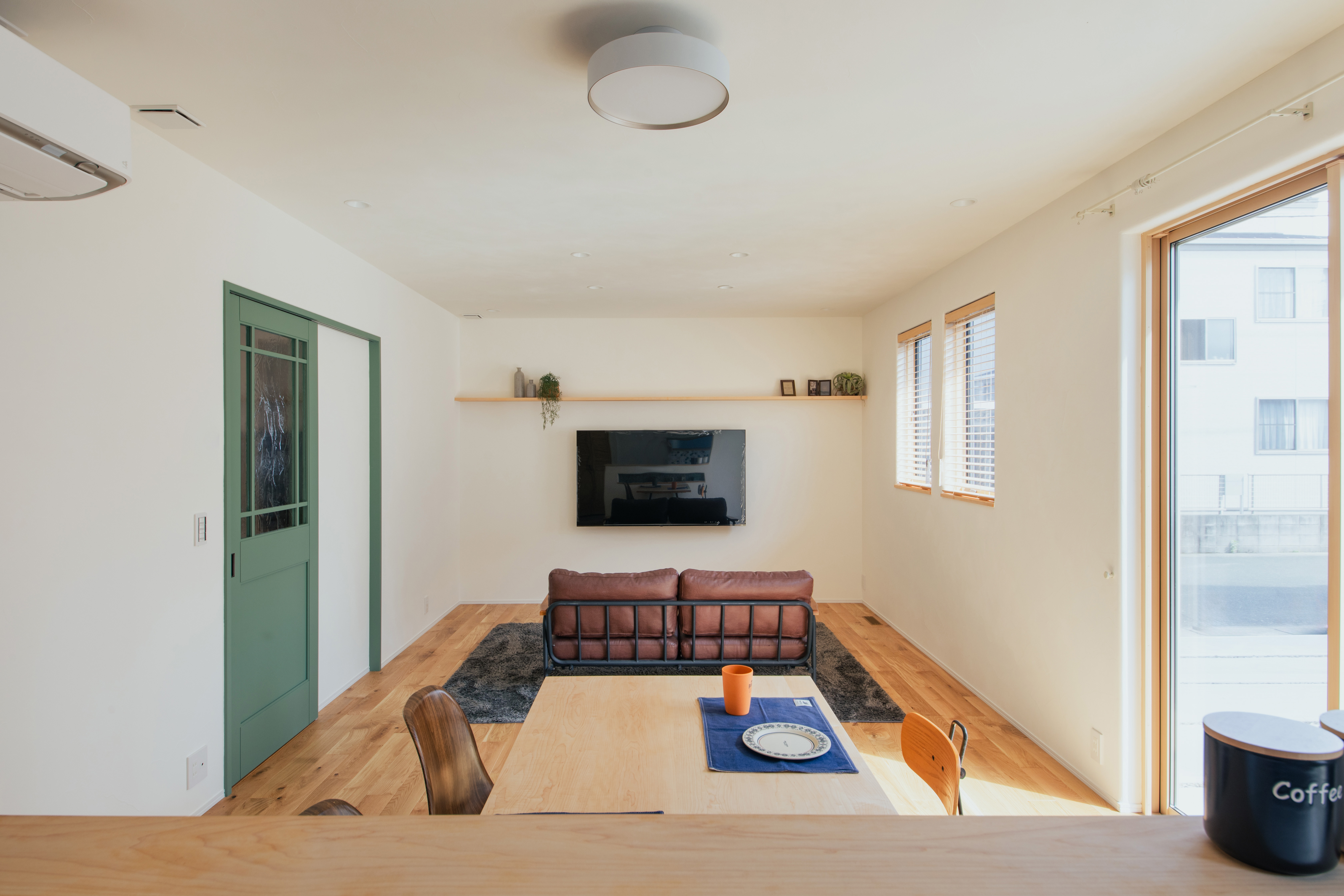 緑のかわいらしい色合いのリビング扉が映えるLDK TVは壁付けですっきりと。その上には、1枚のカウンターを…小物を置いたりと自分色をプラスできる